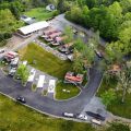 Aerial view of Riverfront ATV Resort showing a curved road lined with RVs, small cabins, and a central building, surrounded by green trees and grassy areas.