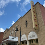 Front of the Granada Theater, a brick building with a tall vertical sign reading 'Granada' and a marquee showing the current movies playing.