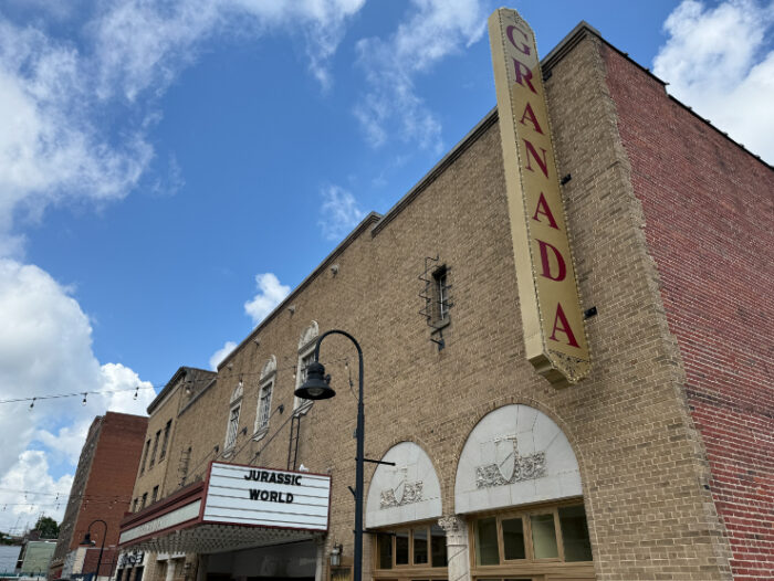 Front of the Granada Theater, a brick building with a tall vertical sign reading 'Granada' and a marquee showing the current movies playing.