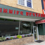 Jimmie's Restaurant storefront with retro red signage, a green and brick exterior, and a window planter with flowers and flags.