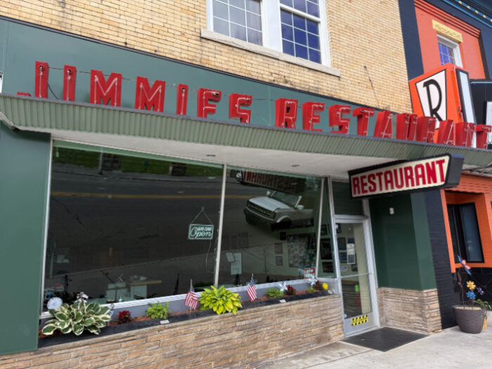 Jimmie's Restaurant storefront with retro red signage, a green and brick exterior, and a window planter with flowers and flags.
