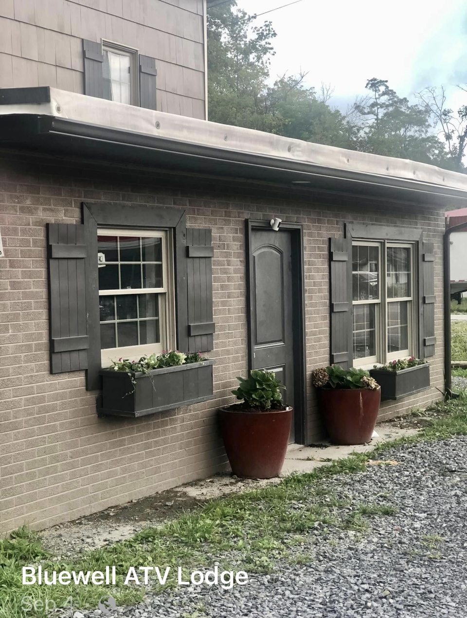 Front view of Bluewell ATV Lodge featuring a tan brick exterior with dark shutters, flower boxes under the windows, and large decorative planters near the entrance.