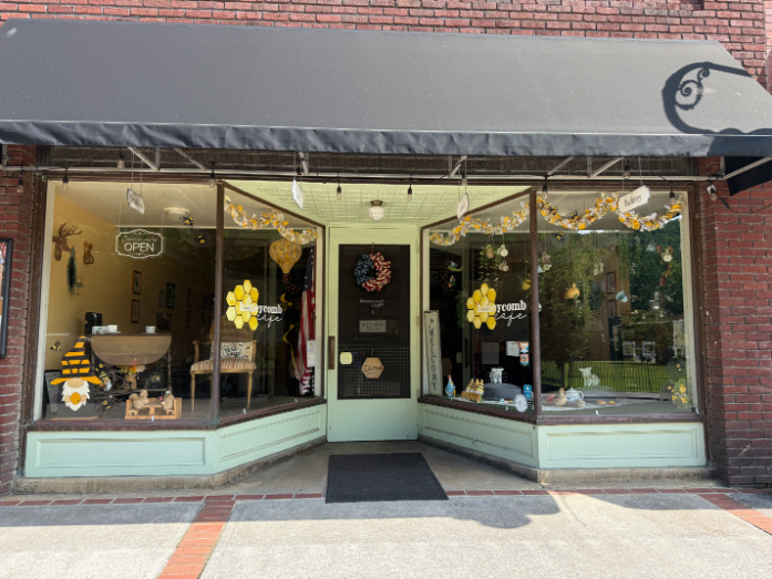 Honeycomb Cafe storefront with large display windows decorated with bees and honeycomb designs, and an 'Open' sign hanging inside.