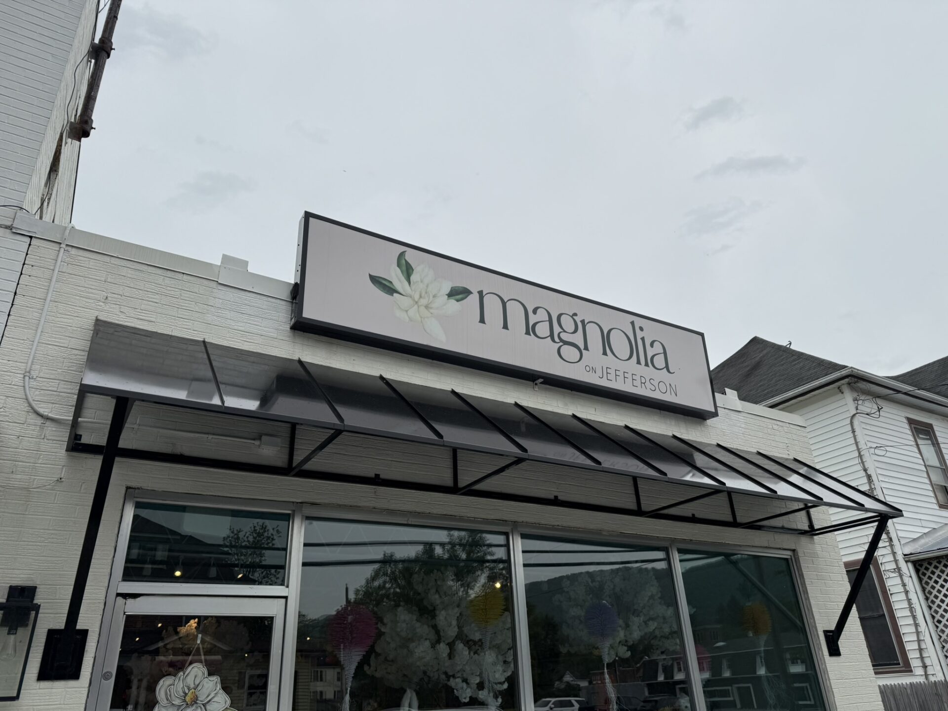 Exterior of Magnolia on Jefferson floral shop with a flower logo on the sign above the large front windows.
