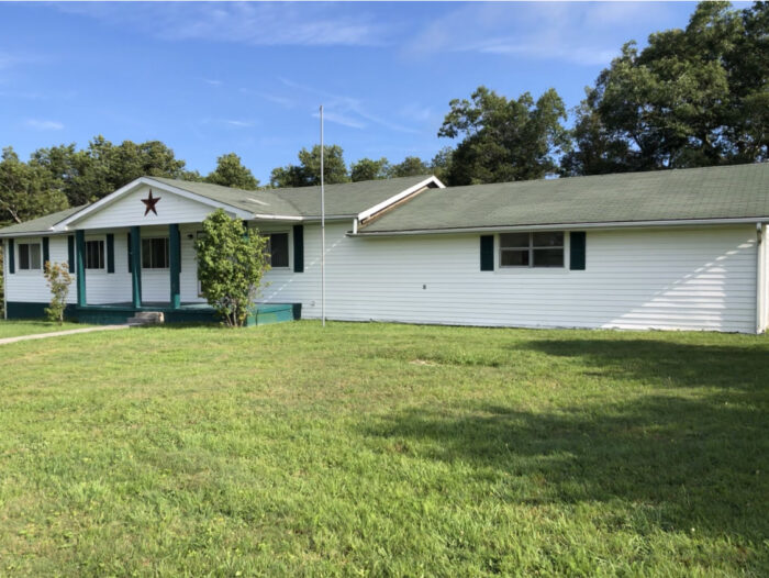 Ashland Retreat, a white single-story house with a large grassy lawn and trees in the background.