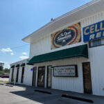 Exterior of Tie Dyed Tarantula, a white building with a colorful tie-dye-themed sign above the entrance and a marquee sign with announcements.