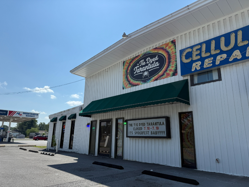 Exterior of Tie Dyed Tarantula, a white building with a colorful tie-dye-themed sign above the entrance and a marquee sign with announcements.