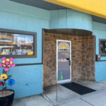 DayDream Games storefront with a stone entrance, bright blue walls, and a colorful flower pot by the door.