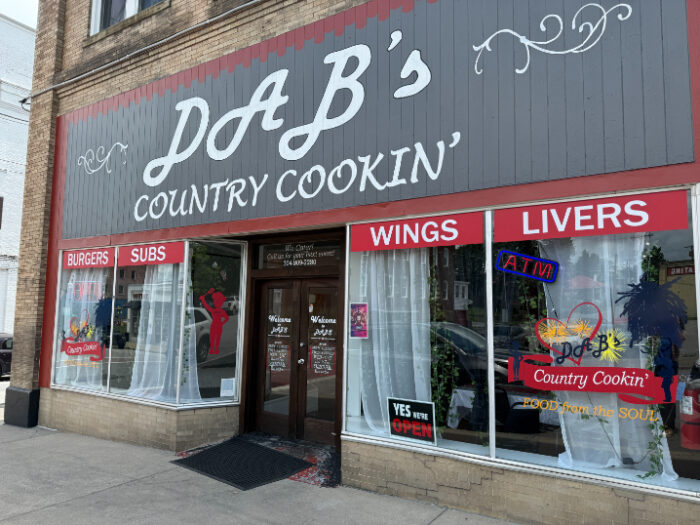 Front of Dab's Country Cookin', a downtown restaurant with a gray and red storefront, large windows, and signage for burgers, subs, wings, and livers.