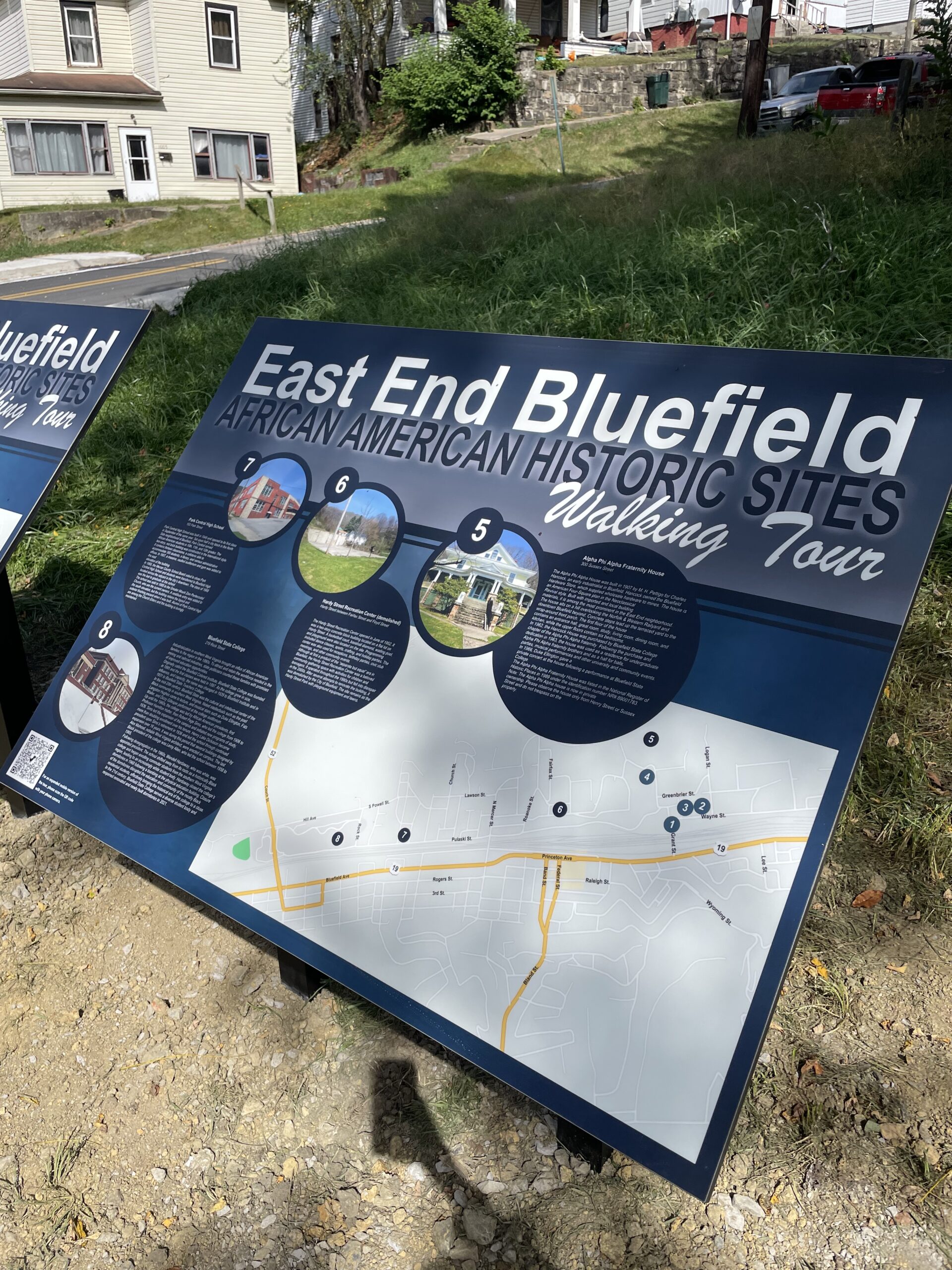 Informational sign for East End Walking Trail Tour, featuring a map and photos of notable locations, mounted outdoors in a grassy area.