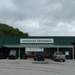 Exterior of Uncharted Adventures, a green metal building with ATVs and enclosed trailers parked out front.