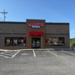 Front view of Teriyaki Madness restaurant with a red awning, brown and tan exterior, and large windows displaying promotional posters.