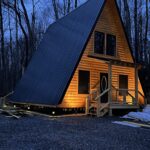 Rock Bottom Cabins A-frame structure with warm lighting, set against a wooden backdrop at dusk.
