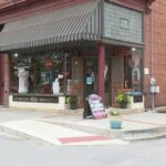 Corner view of Corner Suites, a red brick building with striped awnings and decorative storefront windows, located at a downtown intersection.