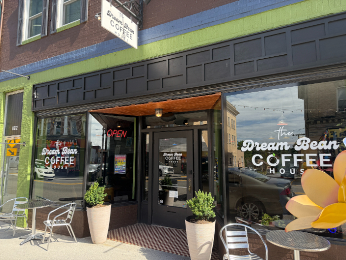 Storefront of the Dream Bean Coffee House with large windows, black trim, potted plants, and outdoor tables with chairs.