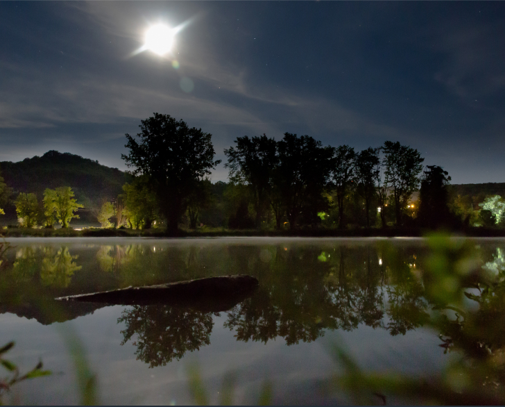 A nighttime image of lake Shawnee. Mist settles in a fine layer over the lake's surface and the moon is visible overhead, casting an eerie glow across the location