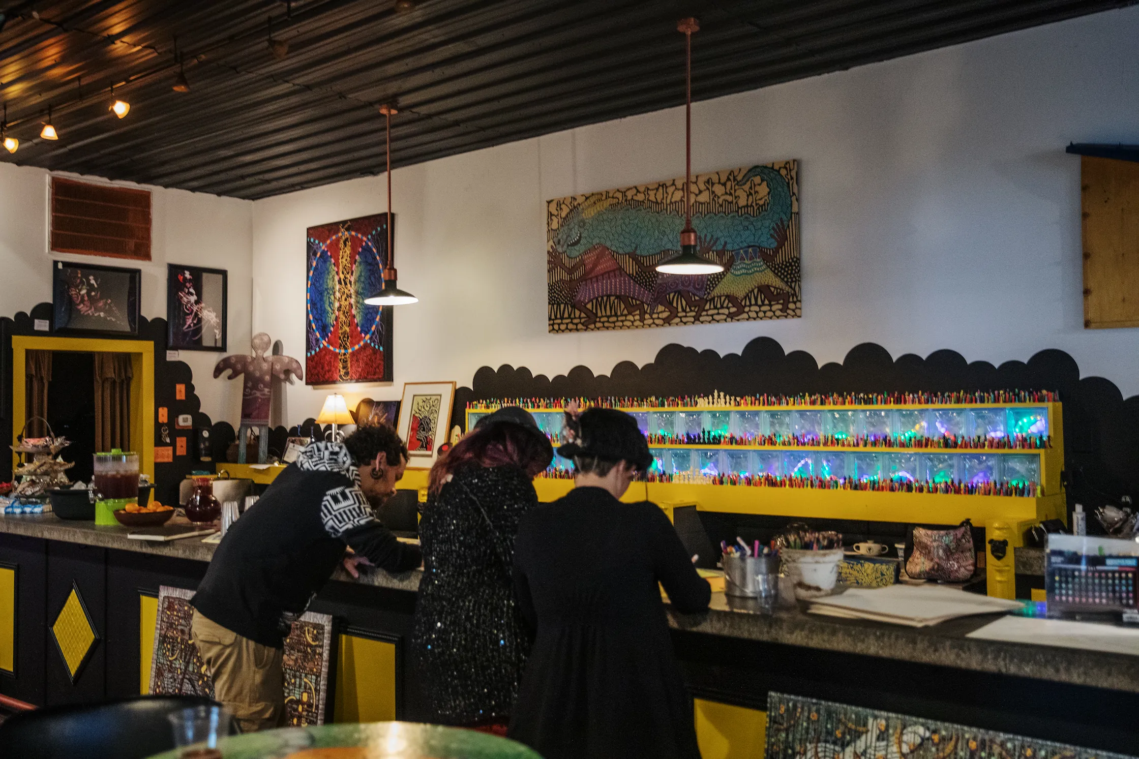 A diverse group of young friends lean against a counter and create artwork with provided materials in a local gallery