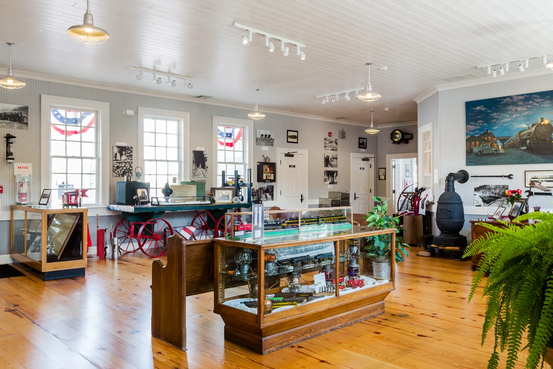 Spacious, bright room with tall windows, white walls, and polished wood floors inside the Princeton Railroad Museum in Mercer County, West Virginia, filled with historic railroad artifacts, photos, and display cases