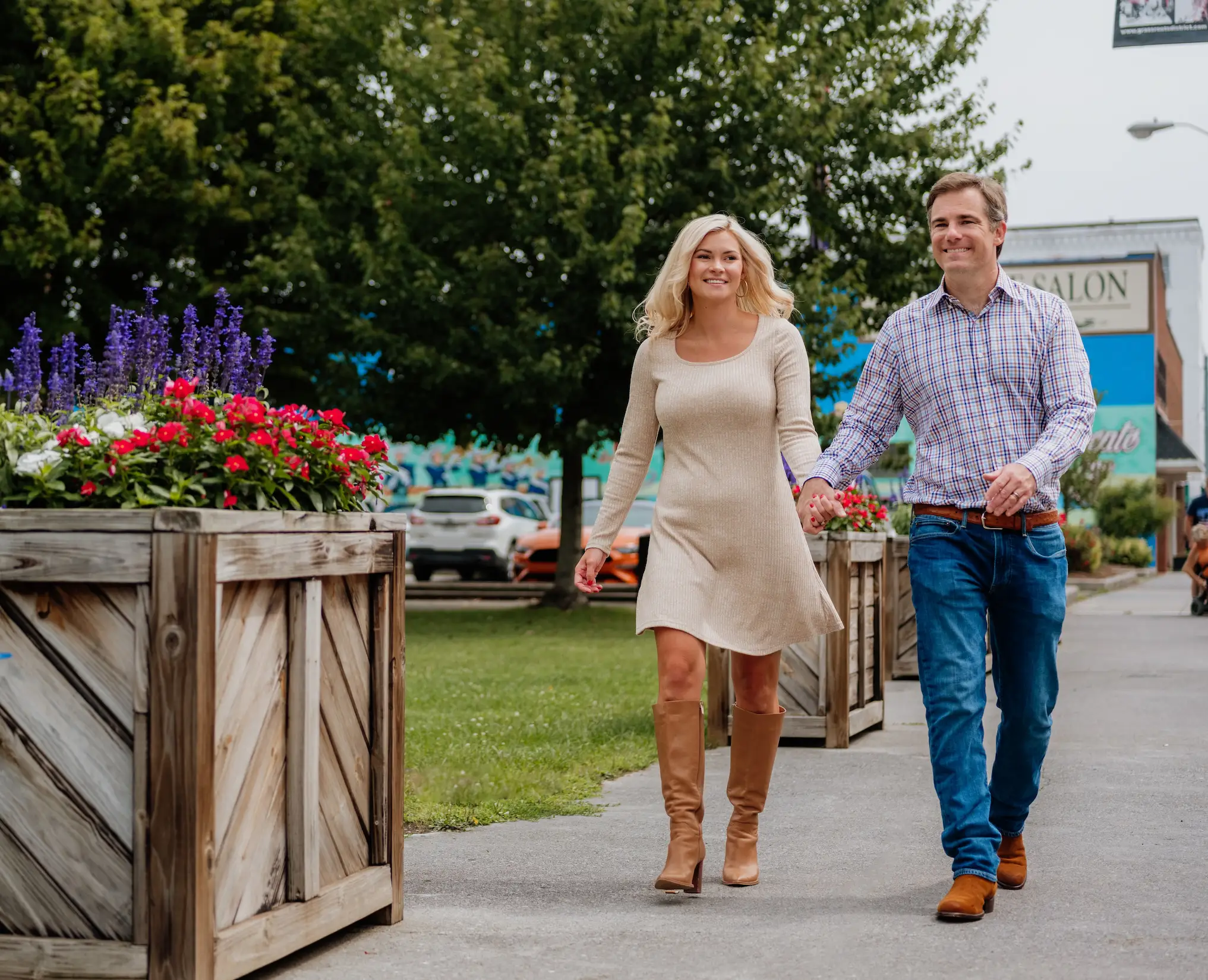 A couple walks hand-in-hand through downtown Mercer County, WV, passing colorful flower planters and local shops on a pleasant day