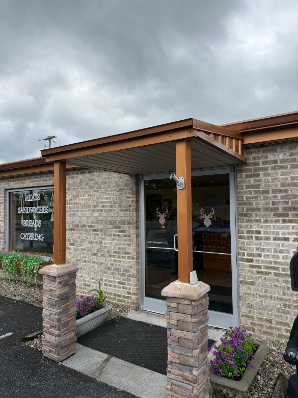 Entrance to Buckland's, a brick building with a small covered porch with wooden beams and stone pillars, featuring glass doors and windows with deer head decals.