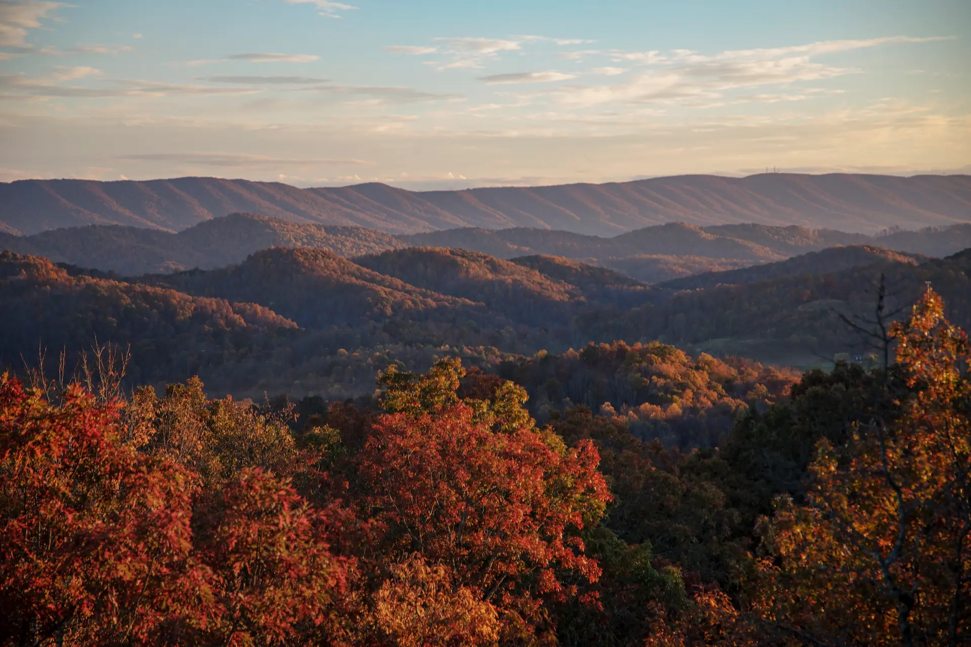 Rolling mountains stretch into the distance in Mercer County, WV, blanketed in vibrant fall foliage under a soft, golden sky at sunset.