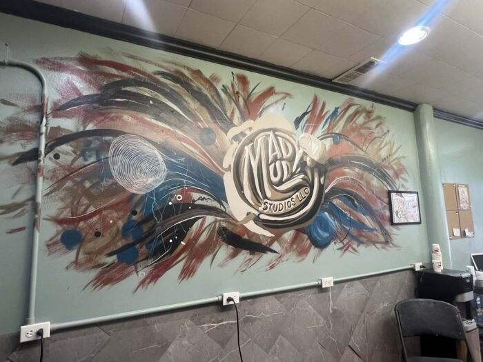 Colorful abstract mural inside Mad Mud Studios LLC featuring bold red, blue, black, and white brushstrokes surrounding a circular “Mad Mud Studios LLC” logo, painted on a light green interior wall