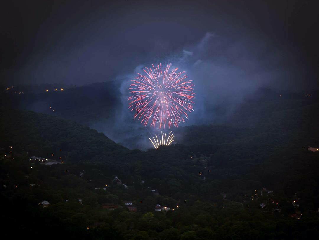 Fireworks burst in the night sky above the dark mountain ridges of Mercer County, West Virginia, during a Fourth of July celebration.
