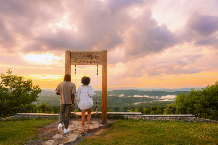 Two visitors walk toward the Almost Heaven Swing at East River Mountain Overlook during a colorful sunset over the Appalachian Mountains in Mercer County, West Virginia.