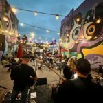 Live music performance at The Number 9 Brewing Company’s outdoor patio in downtown Princeton, WV, with guests seated beneath string lights and colorful murals.