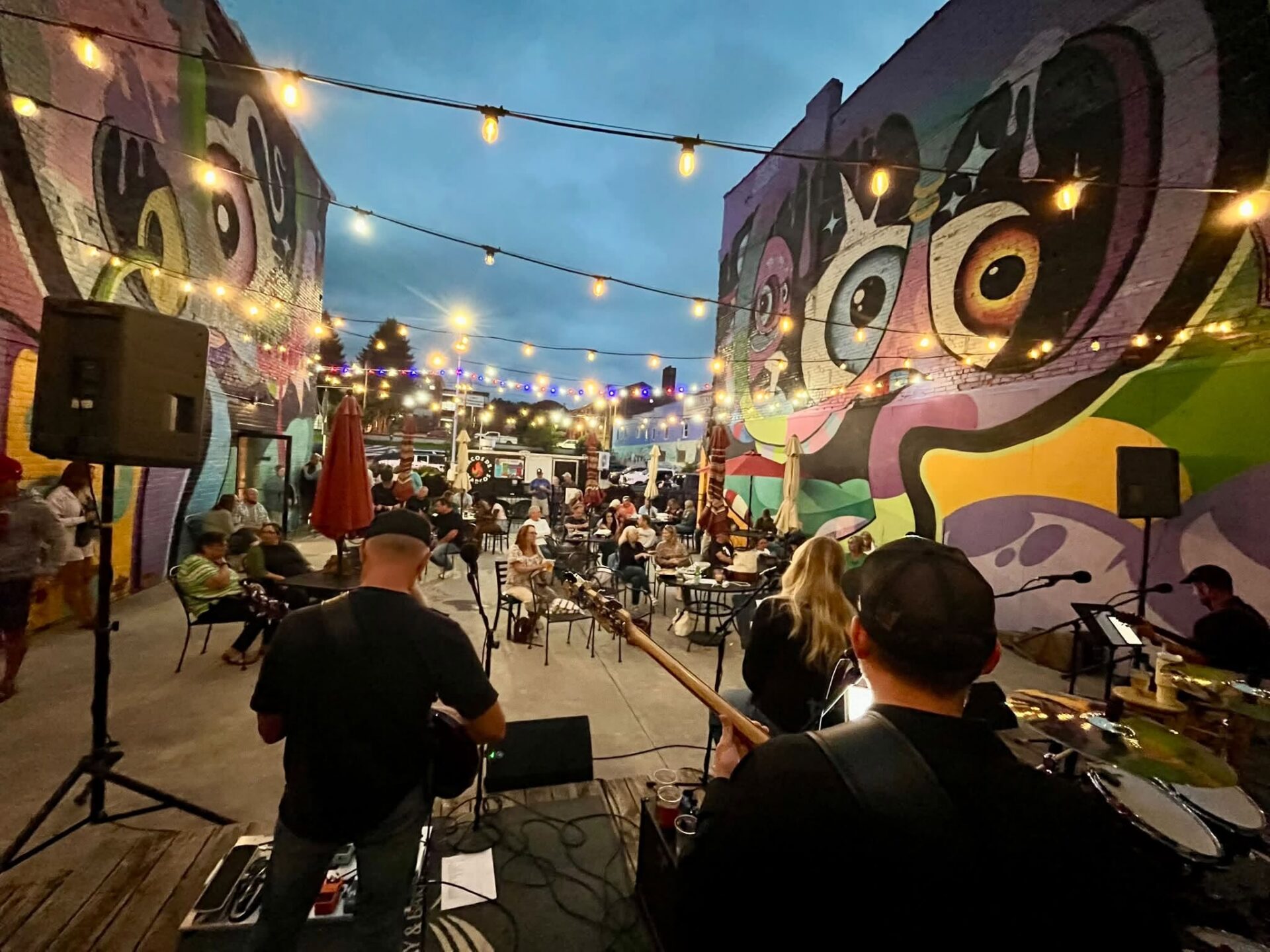 Live music performance at The Number 9 Brewing Company’s outdoor patio in downtown Princeton, WV, with guests seated beneath string lights and colorful murals.